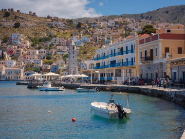 Suriye Adası, Yunanistan - 20 Nisan 2023: Suriye Adası, sakin atmosferli ziyaretçileri hayrete düşüren küçük bir Dodecanese adasıdır. Rengârenk Yunan evlerinin arka planında ada koyunda küçük balıkçı tekneleri