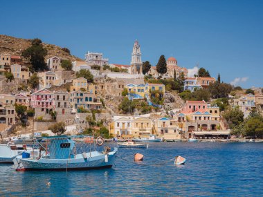 Suriye Adası, Yunanistan - 20 Nisan 2023: Suriye Adası, sakin atmosferli ziyaretçileri hayrete düşüren küçük bir Dodecanese adasıdır. Rengârenk Yunan evlerinin arka planında ada koyunda küçük balıkçı tekneleri
