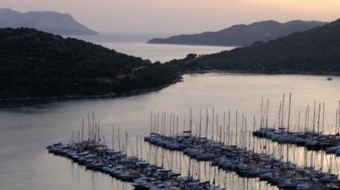 Akdeniz üzerinde gün batımları, Türkiye 'nin Kas kentindeki marinada teknelere altın parıltı saçıyor. Sahne huzurlu ve huzurlu bir akşam vaktidir. Limandaki pek çok lüks tekne ve yatın hava görüntüsü.