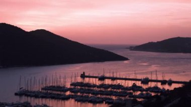 Akdeniz üzerinde gün batımları, Türkiye 'nin Kas kentindeki marinada teknelere altın parıltı saçıyor. Sahne huzurlu ve huzurlu bir akşam vaktidir. Limandaki pek çok lüks tekne ve yatın hava görüntüsü.