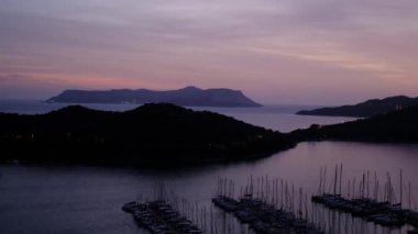 Akdeniz üzerinde gün batımları, Türkiye 'nin Kas kentindeki marinada teknelere altın parıltı saçıyor. Sahne huzurlu ve huzurlu bir akşam vaktidir. Limandaki pek çok lüks tekne ve yatın hava görüntüsü.