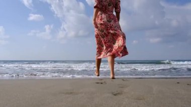 Uçan elbiseli bir kadın Akdeniz sahilinde Antalya, Türkiye 'de Antalya plajında yürürken, sıcak güneş ve hafif esintinin tadını çıkarıyor. Huzur ve memnuniyet içinde, sadece anın tadını çıkarıyor..