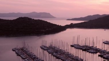 Akdeniz üzerinde gün batımları, Türkiye 'nin Kas kentindeki marinada teknelere altın parıltı saçıyor. Sahne huzurlu ve huzurlu bir akşam vaktidir. Limandaki pek çok lüks tekne ve yatın hava görüntüsü.