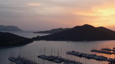 Akdeniz üzerinde gün batımları, Türkiye 'nin Kas kentindeki marinada teknelere altın parıltı saçıyor. Sahne huzurlu ve huzurlu bir akşam vaktidir. Limandaki pek çok lüks tekne ve yatın hava görüntüsü.