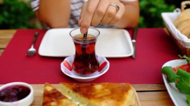 Kadınlar bahçede geleneksel Türk kahvaltısını seviyor. Etrafı yeşilliklerle çevrili bir masada oturuyor. Çay ile şeker karıştıran kadın geleneksel bir Türk çay fincanı olan bardak 'ta