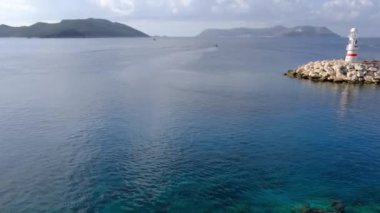 Becon 'la Kas Turkey' in teknesi, ikonik Kas deniz feneri ile Tranquil Körfezi. Gök mavisi suların kıyı sükunetiyle buluştuğu pitoresk cennet,