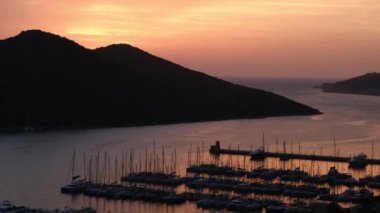 Akdeniz üzerinde gün batımları, Türkiye 'nin Kas kentindeki marinada teknelere altın parıltı saçıyor. Sahne huzurlu ve huzurlu bir akşam vaktidir. Limandaki pek çok lüks tekne ve yatın hava görüntüsü.