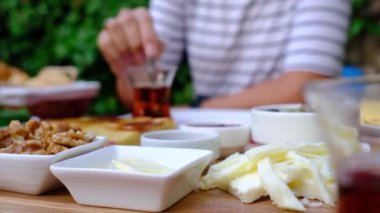 Kadınlar bahçede geleneksel Türk kahvaltısını seviyor. Etrafı yeşilliklerle çevrili bir masada oturuyor. Tabağında taze ekmek, peynir, zeytin, domates, salatalık, yumurta ve bal var. Bir fincan Türk çayı.