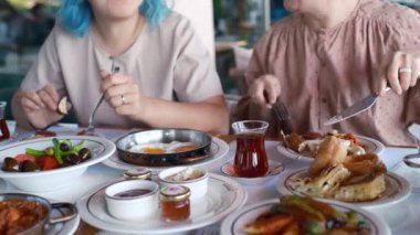 İki kadın yemek yerken gülüyor ve konuşuyor, açıkça görülüyor ki birbirlerinin arkadaşlığından keyif alıyorlar. Türk kahvaltısı, Pazar kahvaltısı veya feta peyniri ve yumurtalı brunch, restoranda Türk yemeği