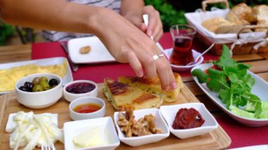 Kadınlar bahçede geleneksel Türk kahvaltısını seviyor. Etrafı yeşilliklerle çevrili bir masada oturuyor. Tabağında taze ekmek, peynir, zeytin, domates, salatalık, yumurta ve bal var. Bir fincan Türk çayı.