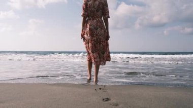 Uçan elbiseli bir kadın Akdeniz sahilinde Antalya, Türkiye 'de Antalya plajında yürürken, sıcak güneş ve hafif esintinin tadını çıkarıyor. Huzur ve memnuniyet içinde, sadece anın tadını çıkarıyor..