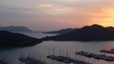 Akdeniz üzerinde gün batımları, Türkiye 'nin Kas kentindeki marinada teknelere altın parıltı saçıyor. Sahne huzurlu ve huzurlu bir akşam vaktidir. Limandaki pek çok lüks tekne ve yatın hava görüntüsü.