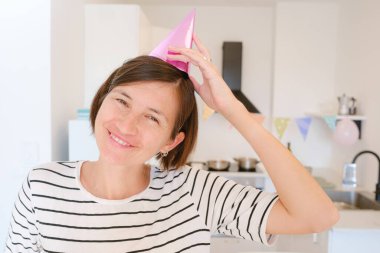 Asyalı kadın doğum gününü evde, rahat bir atmosferde ve şenlikli dekorasyonlarda kutluyor. Pasta, mumlar ve sıcaklıkla geçirdiği özel günün tadını çıkarıyor. Rahatlatıcı ve neşeli anılar yaratıyor.