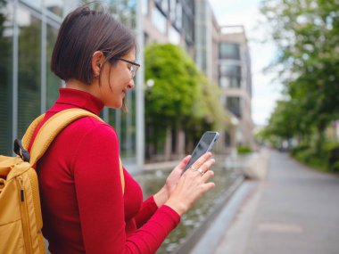 Frankfurt 'taki turist kadın akıllı telefon kullanıyor, daktilo kullanıyor ya da yön arıyor, modern kentsel çevre ile çevrili, hareketli şehirde beklerken teknolojiyle meşgul oluyor..