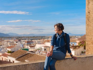 Denia, Alicante, İspanya 'da tarihi şatoyu keşfeden genç bir kadın, aşağıdaki kasabanın manzarası, daha serin mevsim arkaplanlarına karşı. Tarihin ve sükunetin zamansız ortamında harmanlanması.