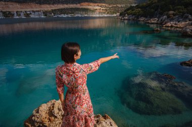 Kadın Akdeniz kıyısında duruyor, soğuk, sezon dışı atmosferi kucaklıyor kıyıya vuran dalgalar ve yukarıdaki bulutlu gökyüzü. Sakin, sakin bir sahilde huzurlu bir an..