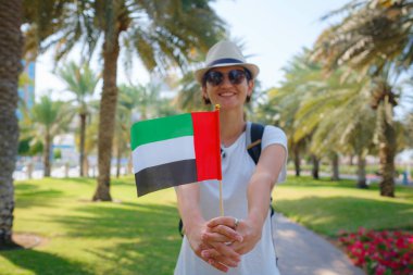 Abu Dabi silueti üzerinde BAE 'nin küçük bayrağını taşıyan kadın Abu Dabi' de gezinti güvertesi. Birleşik Arap Emirlikleri, Orta Doğu. Göçmenlik, öğrenci eğitimi ve Arap Emirlikleri vatandaşlık kavramı