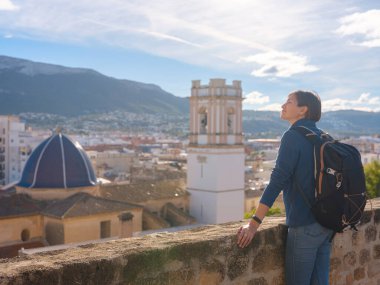 Denia, Alicante, İspanya 'da tarihi şatoyu keşfeden genç bir kadın, aşağıdaki kasabanın manzarası, daha serin mevsim arkaplanlarına karşı. Tarihin ve sükunetin zamansız ortamında harmanlanması.