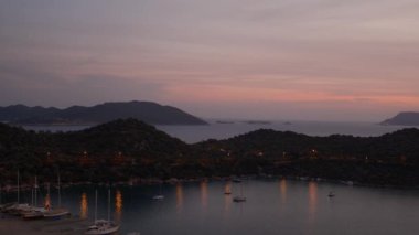 Akdeniz üzerinde gün batımları, Türkiye 'nin Kas kentindeki marinada teknelere altın parıltı saçıyor. Sahne huzurlu ve huzurlu bir akşam vaktidir. Limandaki pek çok lüks tekne ve yatın hava görüntüsü.