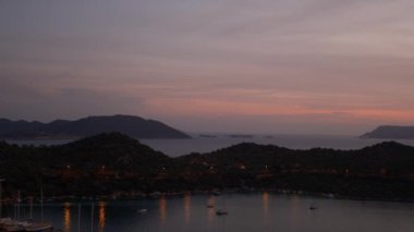 Akdeniz üzerinde gün batımları, Türkiye 'nin Kas kentindeki marinada teknelere altın parıltı saçıyor. Sahne huzurlu ve huzurlu bir akşam vaktidir. Limandaki pek çok lüks tekne ve yatın hava görüntüsü.