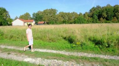 Tarlalar ve ormanlarla çevrili kırsal toprak yolda yürüyen bir adam kırsal hayatın huzurlu ve kırsal atmosferini yakalıyor. Yalnızlığı ve doğayı vurgulayan basit, sessiz bir sahne..