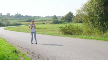 Güneşli bir günde asfalt yolda yürüyen bir kadın yürüyüş macerasına girişiyor. Manzaralı manzaralar ve açık hava ile çevrelenmiş, seyahatin ve açık hava deneyiminin tadını çıkarıyor..