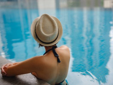 Kuala Lumpur Oteli 'nde havuz başında dinlenen Asyalı genç bir kadın. Etrafı gökdelenlerle çevrili, hareketli şehir ortamında boş vakitlerin tadını çıkarıyor..