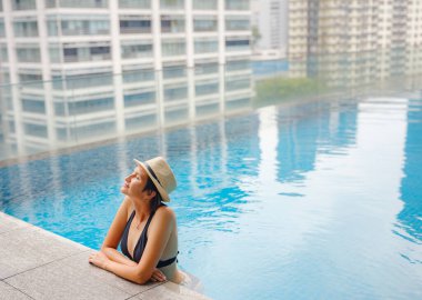 Kuala Lumpur Oteli 'nde havuz başında dinlenen Asyalı genç bir kadın. Etrafı gökdelenlerle çevrili, hareketli şehir ortamında boş vakitlerin tadını çıkarıyor..