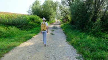 Kırsal alanlarda yürüyüş yapan bir kadın, açık araziler, temiz hava ve huzurlu kırsal manzarayla çevrili. Açık havanın doğal güzelliğini ve sükunetini seviyor..