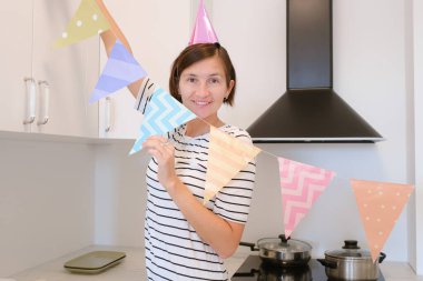 Genç bir kadın, rahat bir atmosfer ve şenlikli dekorasyonla çevrili olarak doğum gününü evde kutluyor. Özel gününün tadını çıkarıyor. Tatile hazırlanıyor, mutfağı dekore ediyor.