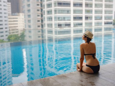 Kuala Lumpur Oteli 'nde havuz başında dinlenen Asyalı genç bir kadın. Etrafı gökdelenlerle çevrili, hareketli şehir ortamında boş vakitlerin tadını çıkarıyor..