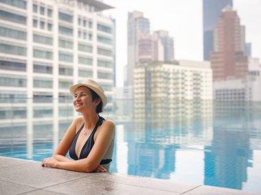 Kuala Lumpur Oteli 'nde havuz başında dinlenen Asyalı genç bir kadın. Etrafı gökdelenlerle çevrili, hareketli şehir ortamında boş vakitlerin tadını çıkarıyor..