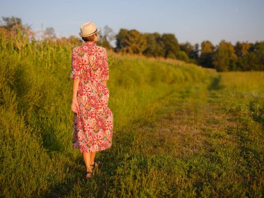Yaz sonlarında Avrupa 'nın pitoresk alanlarında yürüyen genç bir kadın. Altın güneş ışığı, yemyeşil yemyeşil ve sakin kırsal atmosfer huzurlu bir kırsal alan yaratır..