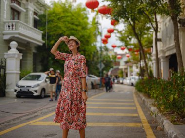 Young woman in ethnic dress and hat exploring the festive streets of George Town, Malaysia, during Chinese New Year. Vibrant lanterns, cultural celebrations, historic charm create unique atmosphere. clipart