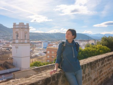 Denia, Alicante, İspanya 'da tarihi şatoyu keşfeden genç bir kadın, aşağıdaki kasabanın manzarası, daha serin mevsim arkaplanlarına karşı. Tarihin ve sükunetin zamansız ortamında harmanlanması.