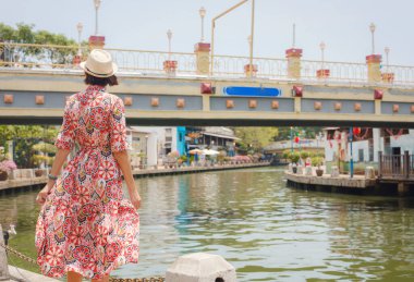 Malacca, Malezya 'nın canlı sokaklarını keşfeden etnik giysili ve şapkalı genç bir kadın. Kültürel miras, renkli mimari ve tropikal cazibenin bir karışımı. Mükemmel seyahat ve yaşam tarzı anları.