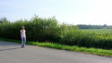 Güneşli bir günde asfalt yolda yürüyen bir kadın yürüyüş macerasına girişiyor. Manzaralı manzaralar ve açık hava ile çevrelenmiş, seyahatin ve açık hava deneyiminin tadını çıkarıyor..