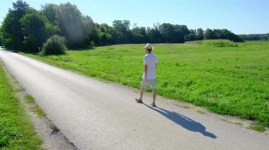 Tarlalar ve ormanlarla çevrili asfalt yolda yürüyen bir adam yalnızlık ve sükunet hissini yakalıyor. Açık alan ve yeşillik ile kırsal alan huzurlu ve düşünceli bir manzara yaratır..