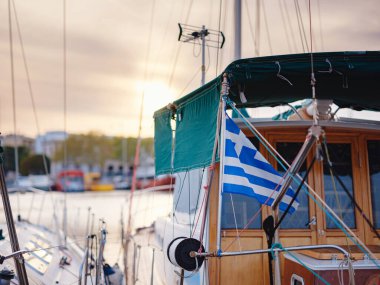 View of Greek flag waving in air serene Mediterranean vibe. beautiful Greek islands series, sailing yacht in harbour offering tourists daily cruises along side Greek flag. clipart