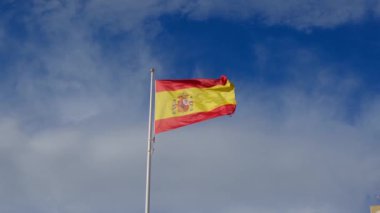 İspanyol bayrağı zarif bir şekilde mavi gökyüzüne doğru dalgalanıyor. Spains kültürel kimliğinin özünü yakalayan ulusal gurur, birlik ve mirasın güçlü bir sembolü.