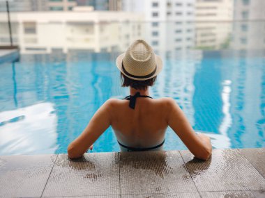 Kuala Lumpur Oteli 'nde havuz başında dinlenen Asyalı genç bir kadın. Etrafı gökdelenlerle çevrili, hareketli şehir ortamında boş vakitlerin tadını çıkarıyor..