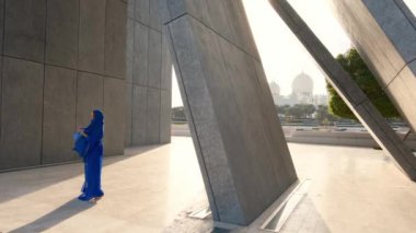 Abu Dabi 'deki Şeyh Zayed Büyük Camii yakınlarındaki Wahat Al Karama' daki geleneksel Arap elbiseli kadın, gün batımında kültürel zarafet ve ikonik İslami mimari sergiliyor..