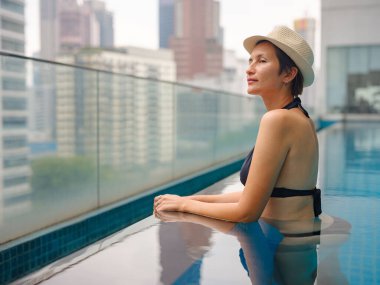 Kuala Lumpur Oteli 'nde havuz başında dinlenen Asyalı genç bir kadın. Etrafı gökdelenlerle çevrili, hareketli şehir ortamında boş vakitlerin tadını çıkarıyor..