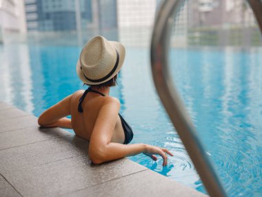 Kuala Lumpur Oteli 'nde havuz başında dinlenen Asyalı genç bir kadın. Etrafı gökdelenlerle çevrili, hareketli şehir ortamında boş vakitlerin tadını çıkarıyor..