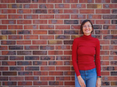 Gözlüklü ve kırmızı balıkçı yakalı bir kadın, iş stili giyinmiş, Frankfurt 'un merkezinde duruyor, modern binalar ve şehir hayatı ile çevrili, profesyonellik ve özgüvenin vücut bulmuş hali.