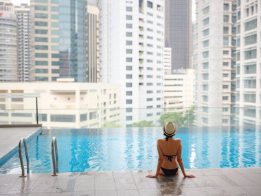 Kuala Lumpur Oteli 'nde havuz başında dinlenen Asyalı genç bir kadın. Etrafı gökdelenlerle çevrili, hareketli şehir ortamında boş vakitlerin tadını çıkarıyor..