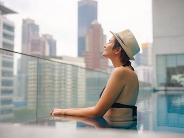 Kuala Lumpur Oteli 'nde havuz başında dinlenen Asyalı genç bir kadın. Etrafı gökdelenlerle çevrili, hareketli şehir ortamında boş vakitlerin tadını çıkarıyor..