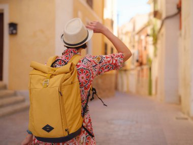İspanyol kıyı kasabası La Vila Joiosa 'nın renkli sokaklarında gezen kadın. Güneşli kış atmosferi Akdeniz mimarisinin cazibesini ve sakin sahil yaşamını ön plana çıkarıyor.