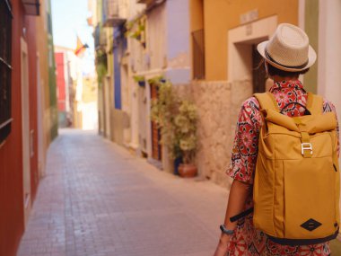 İspanyol kıyı kasabası La Vila Joiosa 'nın renkli sokaklarında gezen kadın. Güneşli kış atmosferi Akdeniz mimarisinin cazibesini ve sakin sahil yaşamını ön plana çıkarıyor.