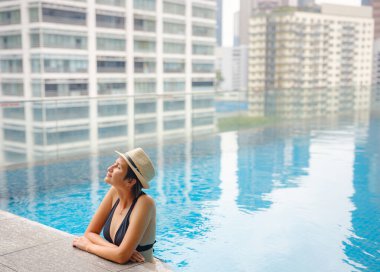 Kuala Lumpur Oteli 'nde havuz başında dinlenen Asyalı genç bir kadın. Etrafı gökdelenlerle çevrili, hareketli şehir ortamında boş vakitlerin tadını çıkarıyor..